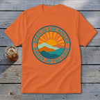 An orange crewneck t-shirt featuring a retro mountain and sun graphic with text reading Born in the Holler Raised on the Ridge.