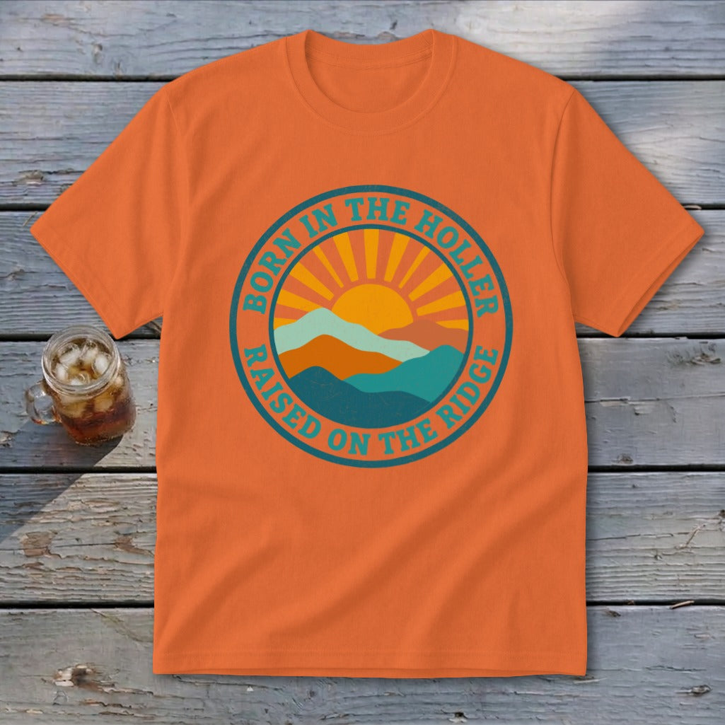 An orange crewneck t-shirt featuring a retro mountain and sun graphic with text reading Born in the Holler Raised on the Ridge.