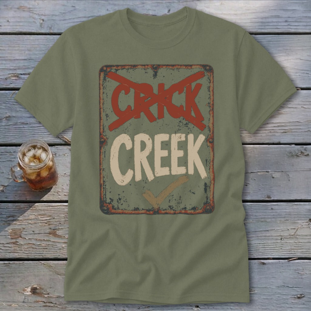 Olive green t-shirt with distressed sign graphic reading "CRICK" crossed out and "CREEK" with a checkmark.