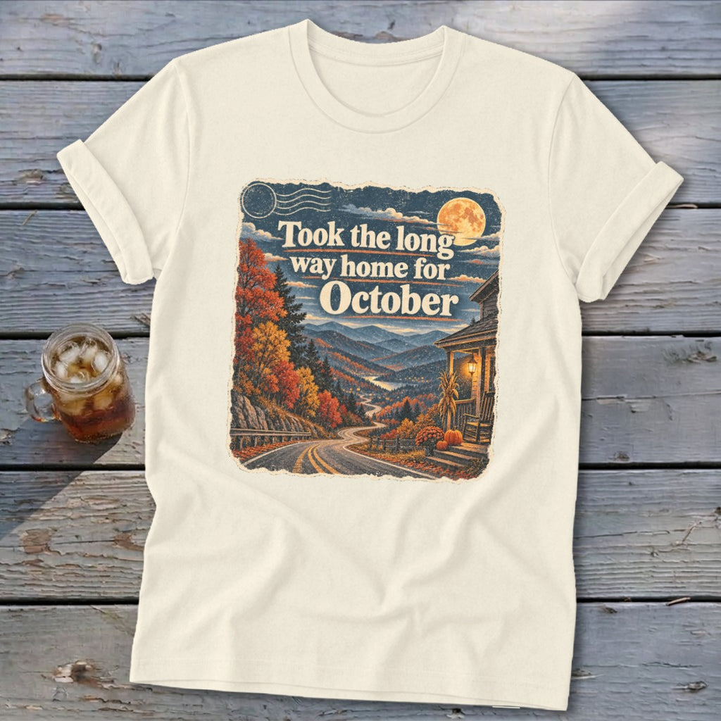 Cream t-shirt with graphic of autumn mountains, winding road, house, and text "Took the long way home for October."