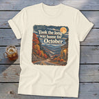 Cream t-shirt with graphic of autumn mountains, winding road, house, and text "Took the long way home for October."