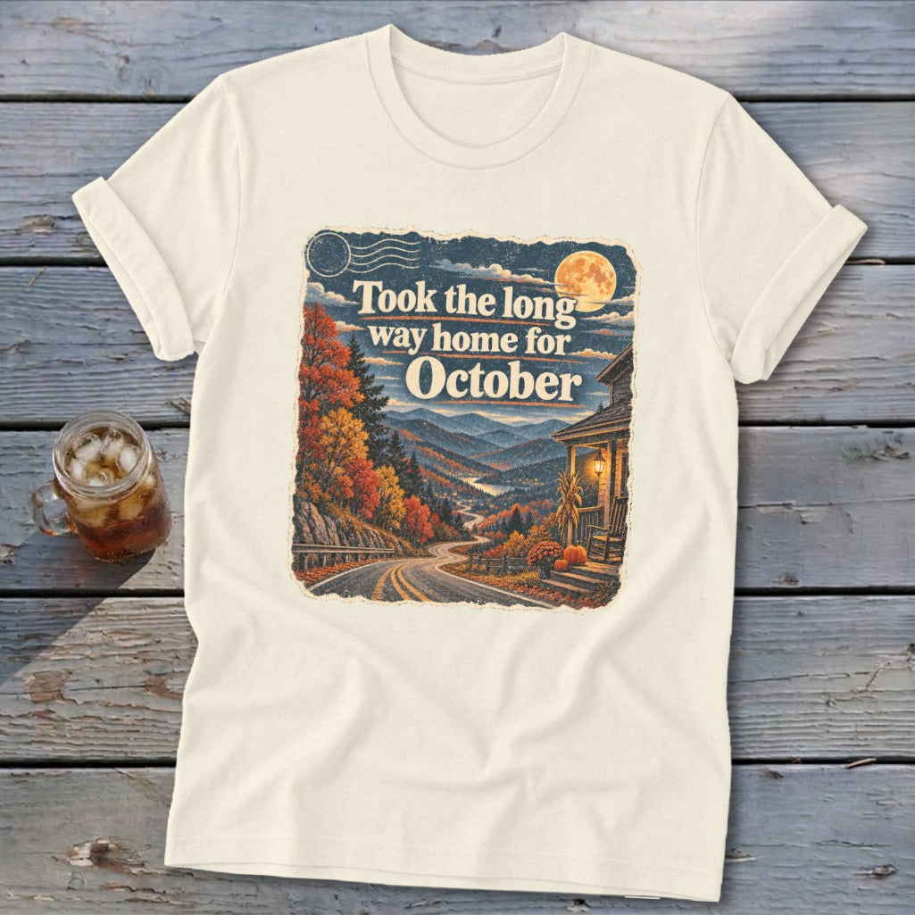 Cream t-shirt with graphic of autumn mountains, winding road, house, and text "Took the long way home for October."