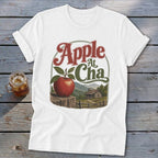 A white t-shirt featuring a graphic with an apple, a cabin, mountains, and the text Apple At Cha.