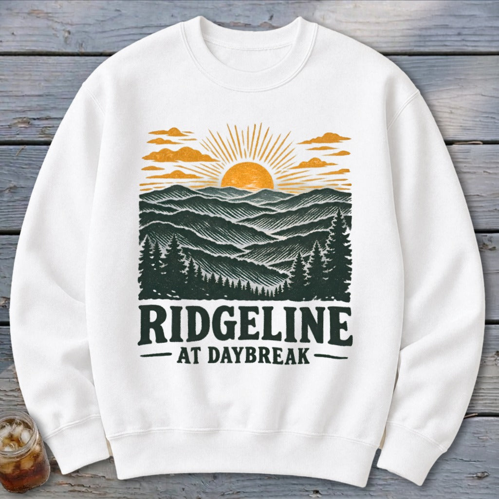 White sweatshirt with "RIDGELINE AT DAYBREAK" text and a mountain sunrise graphic.