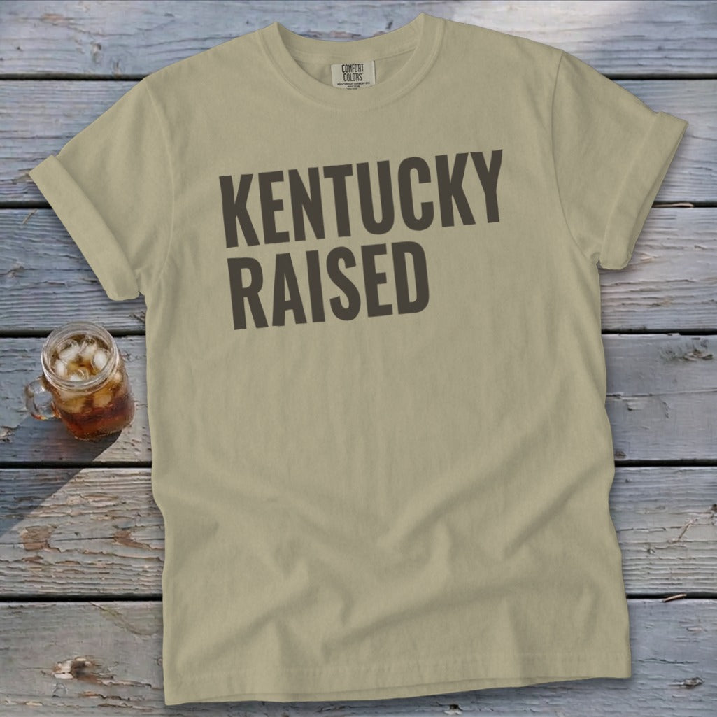 T-shirt with "KENTUCKY RAISED" text in dark grey on a tan background.