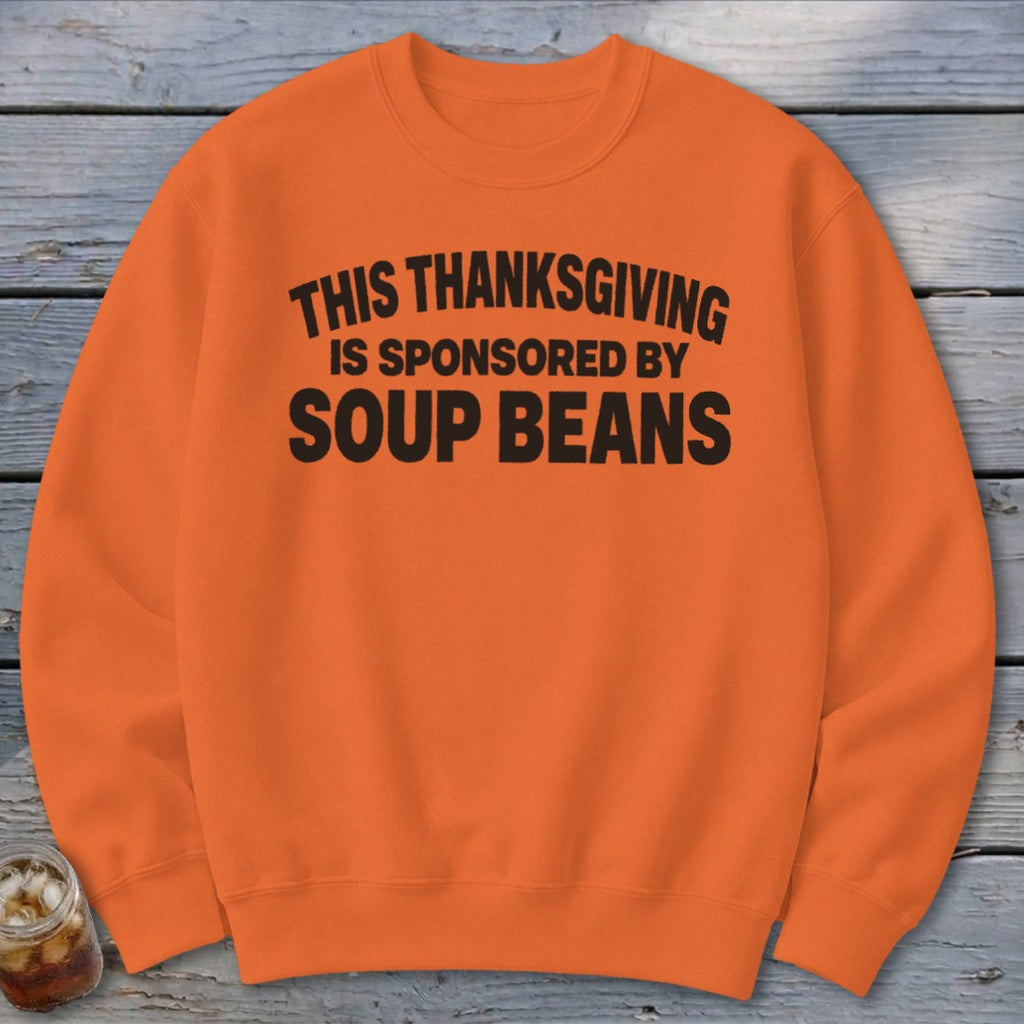 Orange crewneck sweatshirt featuring black text reading THIS THANKSGIVING IS SPONSORED BY SOUP BEANS.