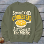 Olive green crewneck sweatshirt featuring a graphic of yellow cornbread in a skillet and text that reads, "Some of Y'all's Cornbread Ain't Done in the Middle."