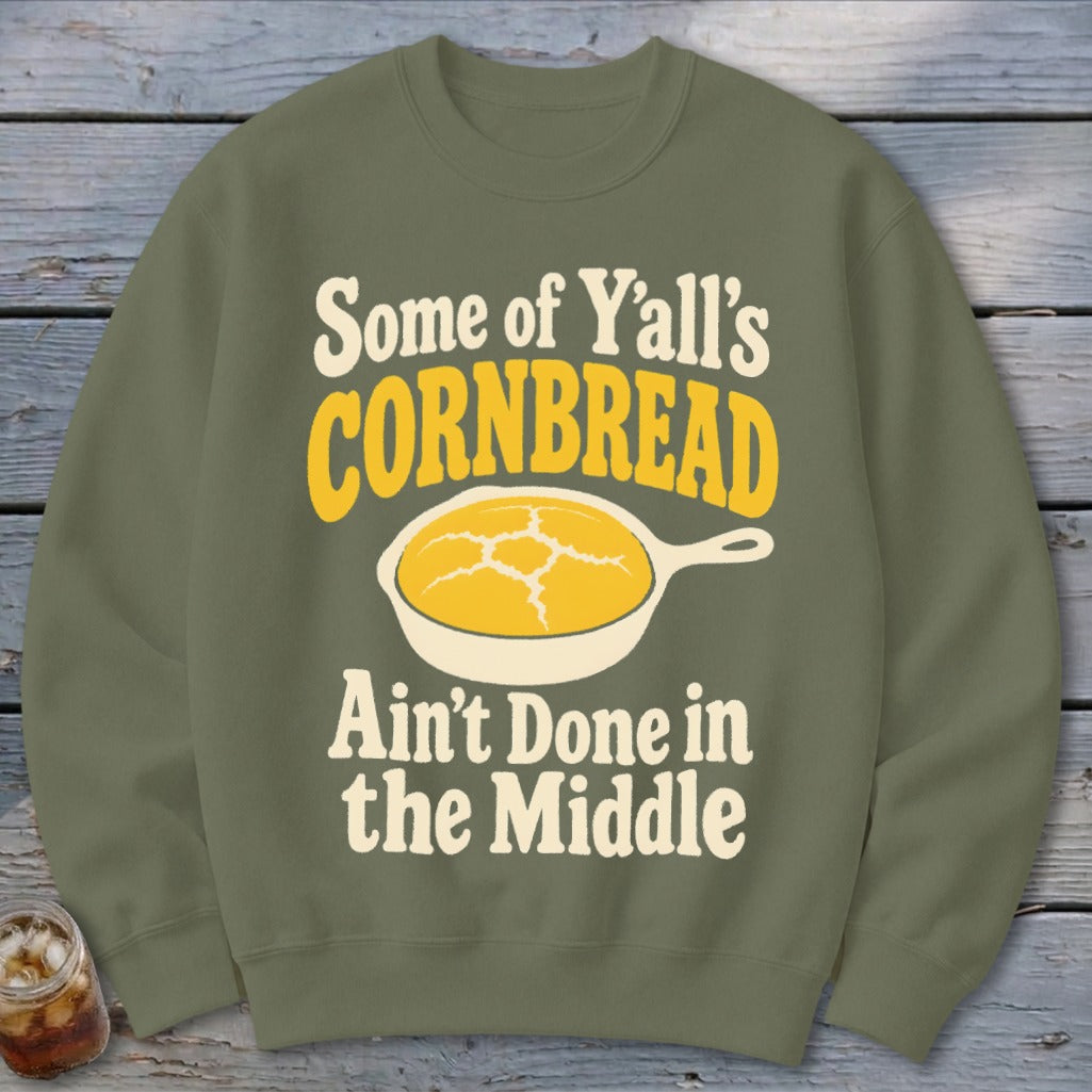 Olive green crewneck sweatshirt featuring a graphic of yellow cornbread in a skillet and text that reads, "Some of Y'all's Cornbread Ain't Done in the Middle."
