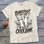 Cream t-shirt with black graphic of bare feet in water and text "Barefoot on the Crick Bank".