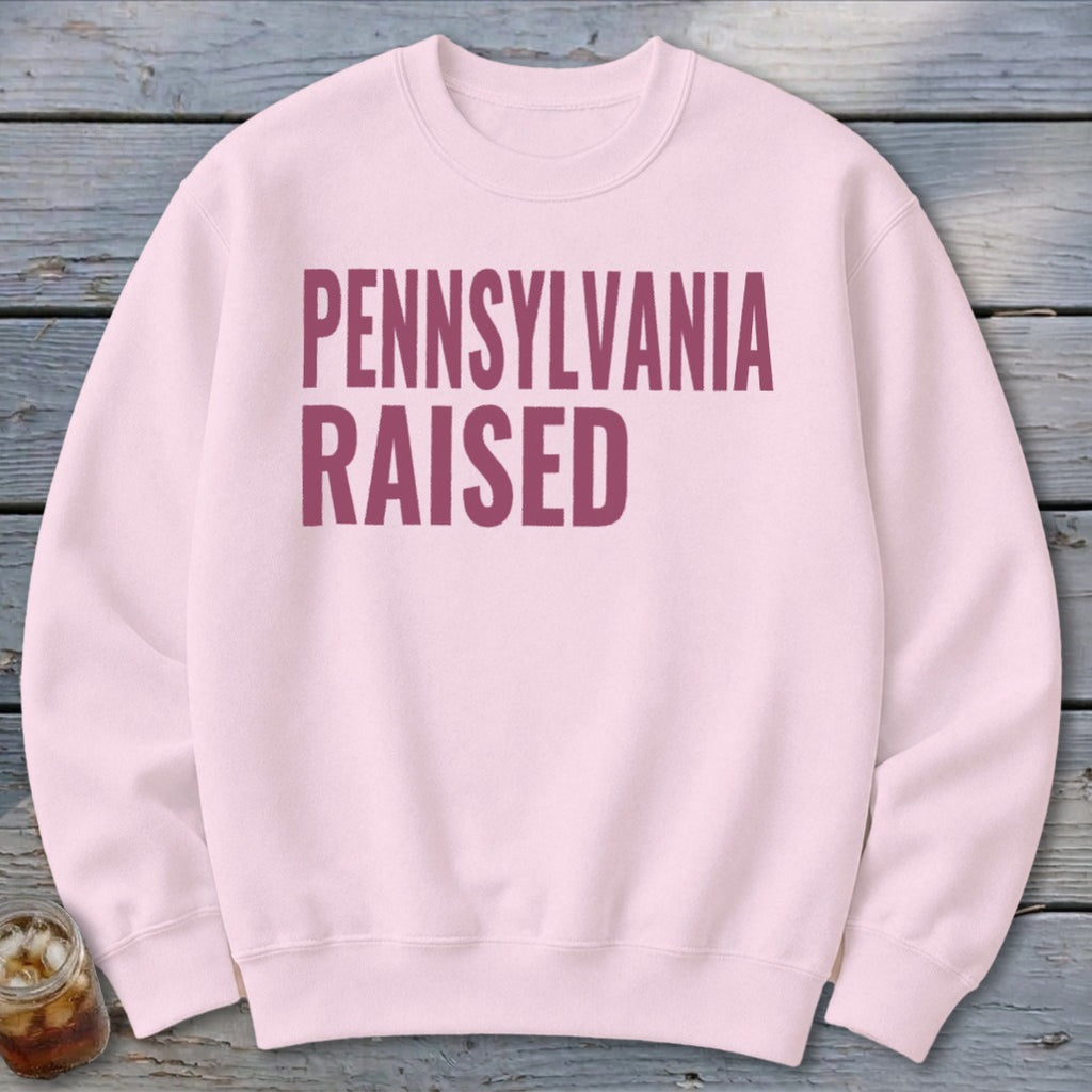 Pink crewneck sweatshirt with bold maroon text reading "PENNSYLVANIA RAISED".
