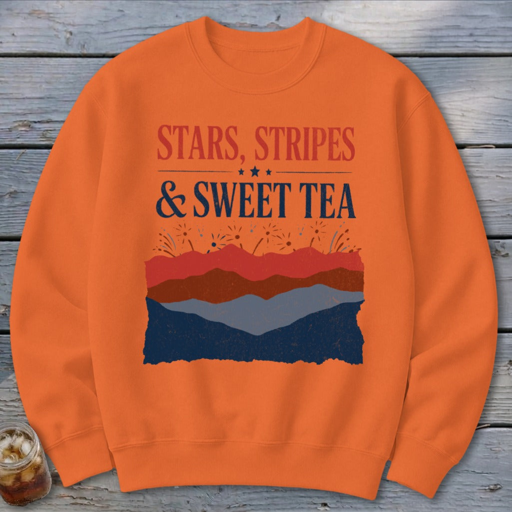 Bright orange crewneck sweatshirt featuring red and blue patriotic text and layered mountain graphics.