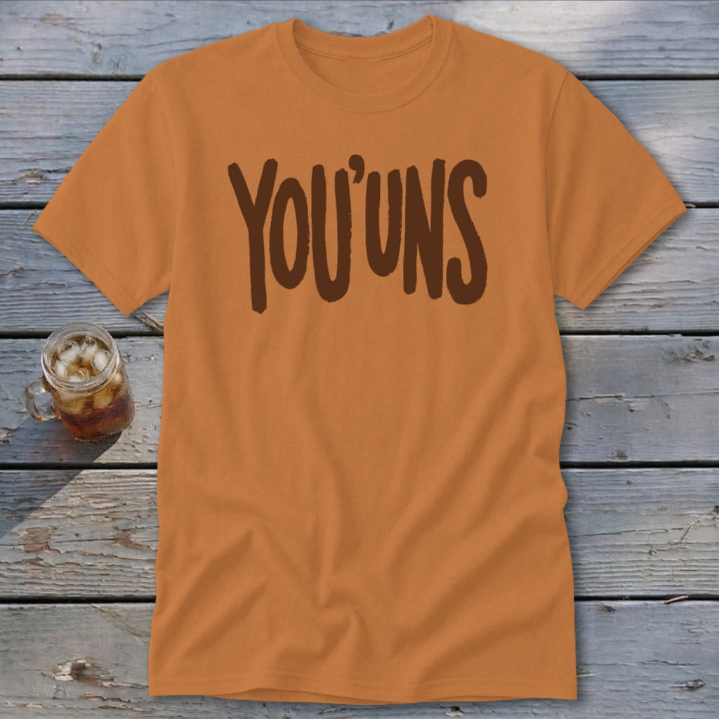 Orange t-shirt with "YOU'UNS" text in brown, next to a glass of iced tea.