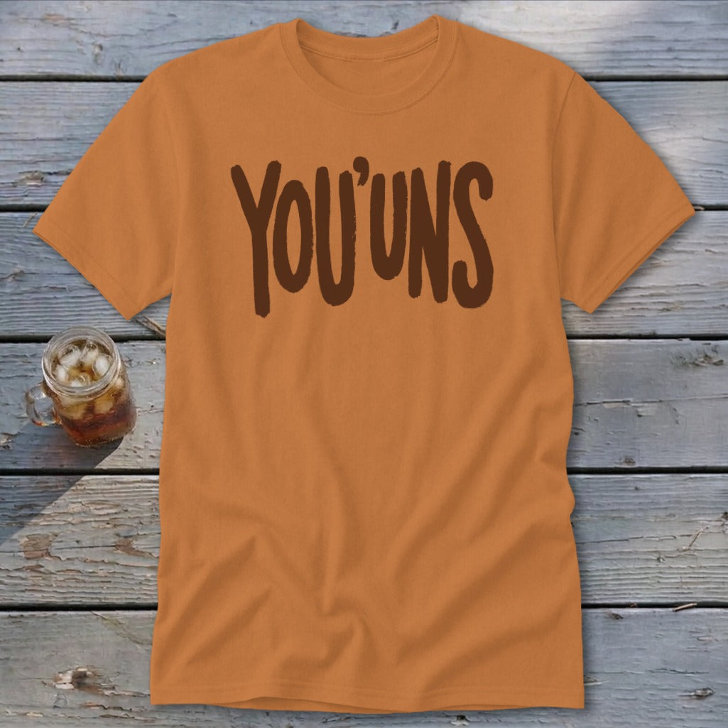 Orange t-shirt with "YOU'UNS" text in brown, next to a glass of iced tea.