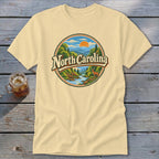 Light yellow t-shirt with circular "North Carolina" graphic featuring mountains, trees, and a deer.