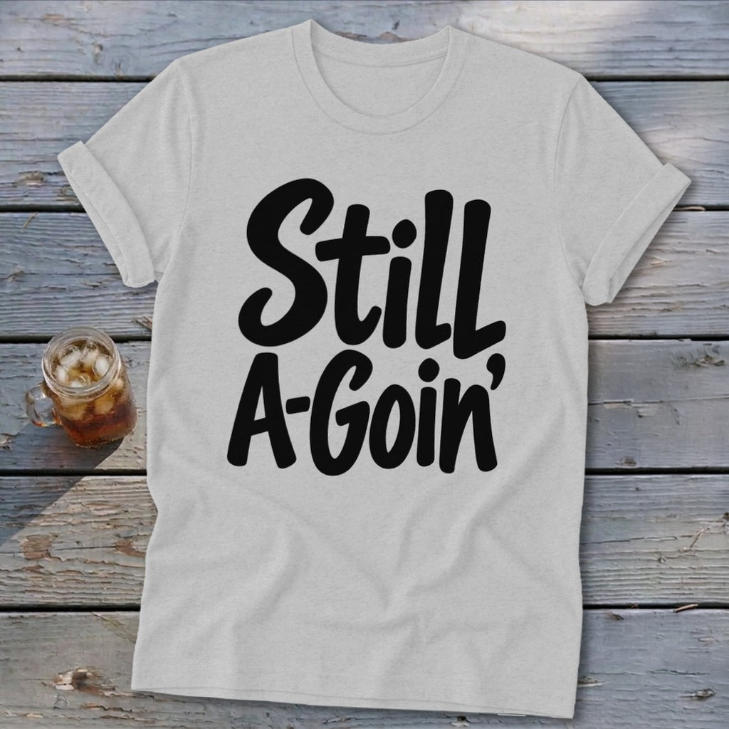Heather gray crewneck t-shirt with rolled sleeves featuring the black text Still A-Goin' on a wooden background.