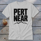 Light gray t-shirt with black Pert Near text and a mountain silhouette on a wooden surface.