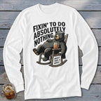 A white long-sleeved t-shirt with a graphic of a bear sleeping in a rocking chair, holding a drink, with the text "FIXIN' TO DO ABSOLUTELY NOTHING, MIGHT TAKE A WHILE."