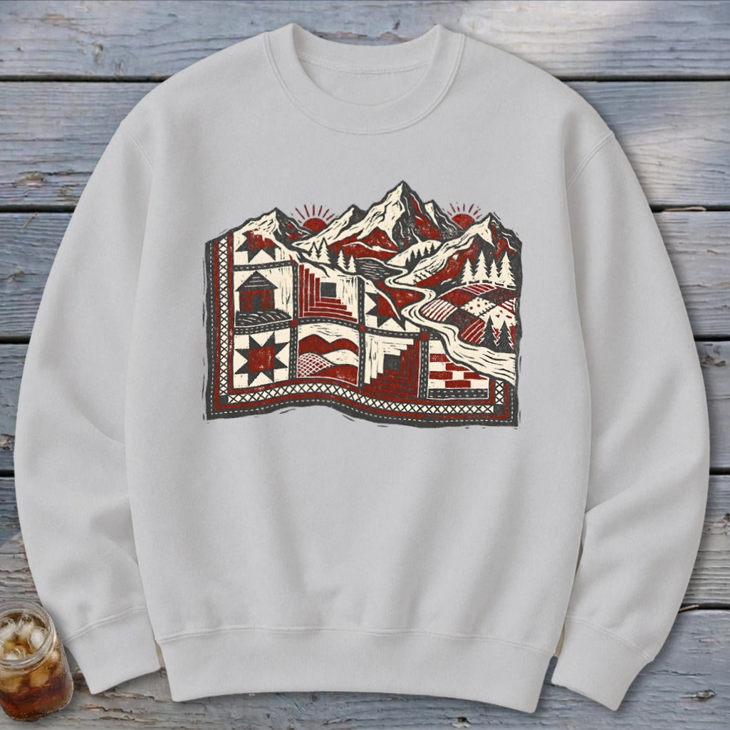 Light gray crewneck sweatshirt featuring a patchwork quilt graphic blending mountain landscape imagery in red, black, and white.