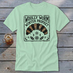 A light green t-shirt displays a black graphic featuring a woolly worm and the text Woolly Worm Winter Prophet.