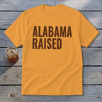 Orange t-shirt with brown text reading "ALABAMA RAISED".