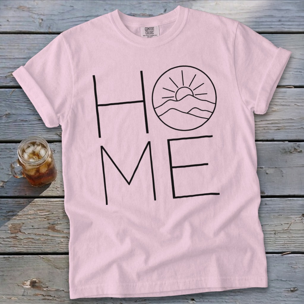 Light pink t-shirt with black text reading "HOME," featuring a mountain and sun graphic inside the letter O.