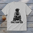 White t-shirt with black graphic of boy in overalls and cap holding a bucket, "Coal Camp Kid" text.