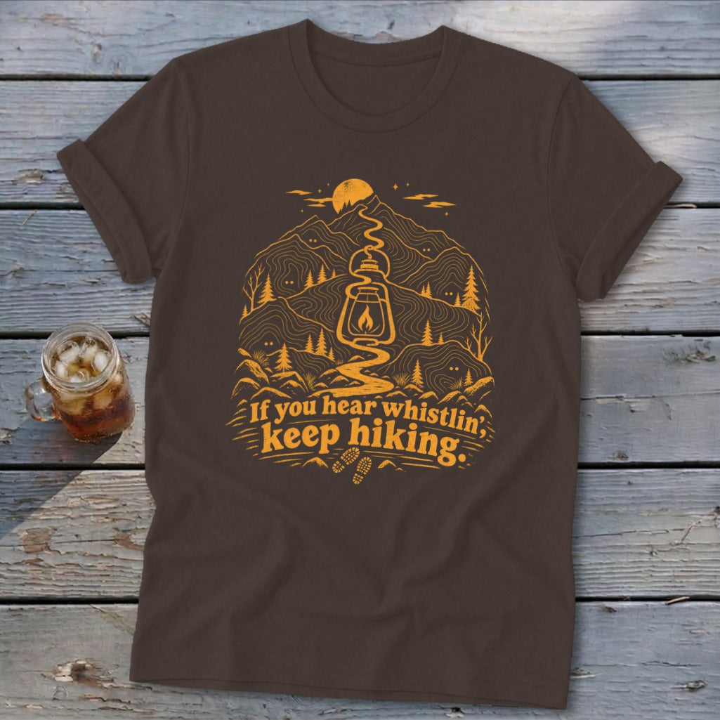 Brown t-shirt with orange graphic of lantern, mountains, and text "If you hear whistlin', keep hiking."