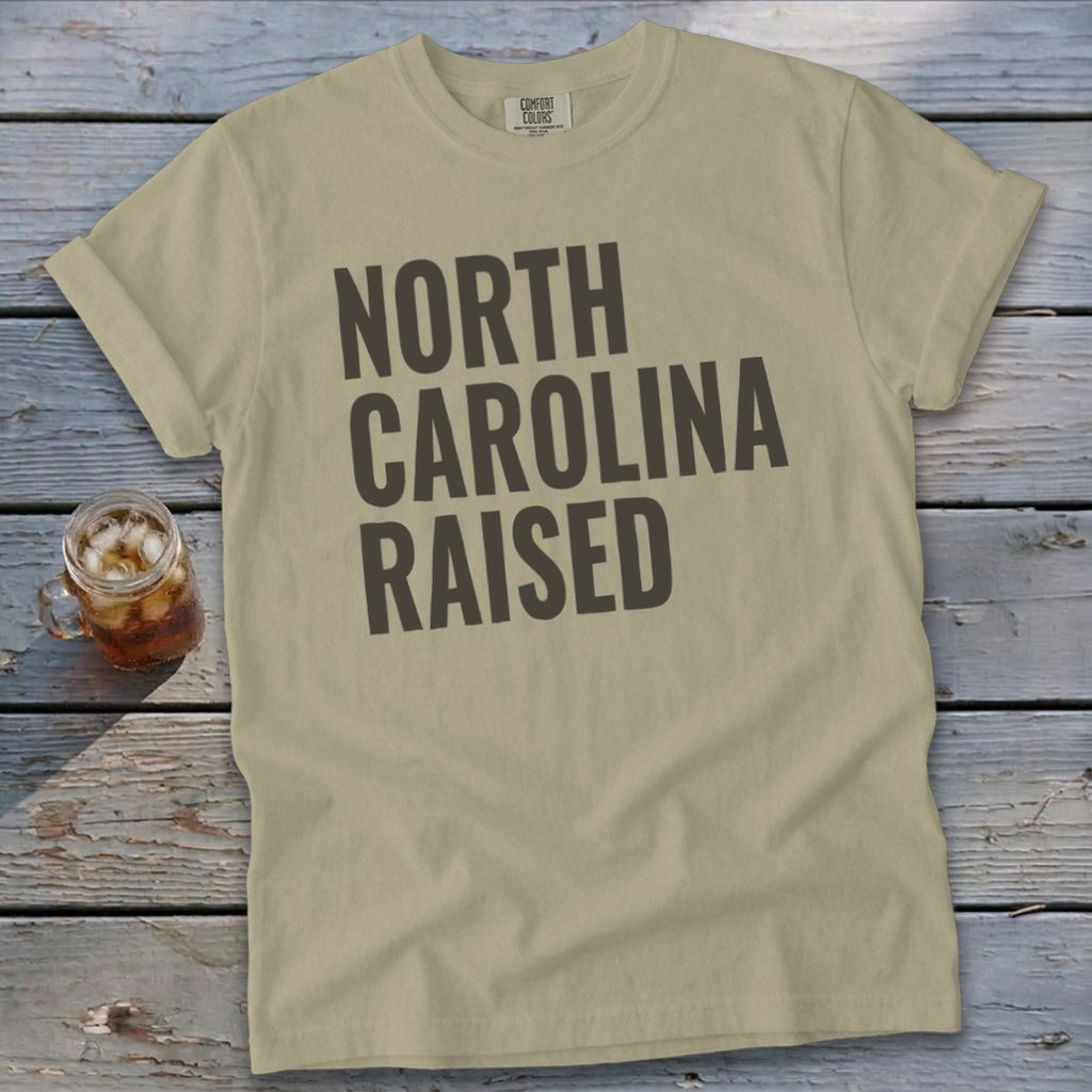 Tan t-shirt with "NORTH CAROLINA RAISED" printed in dark gray text.