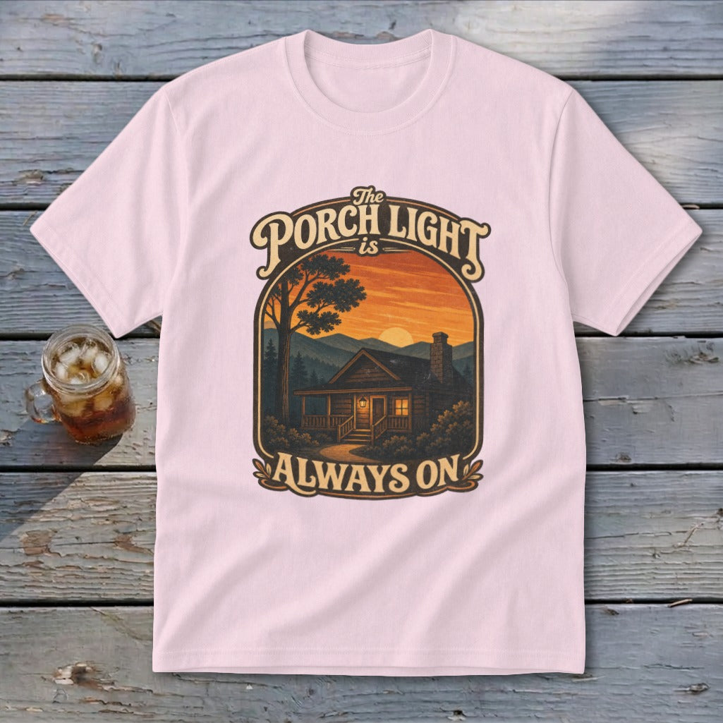 Pink t-shirt with cabin and sunset graphic, reading "The Porch Light is Always On".