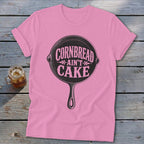 Pink t-shirt with black graphic of a cast iron skillet reading "Cornbread Ain't Cake".