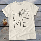 Cream crewneck t-shirt featuring the word HOME in black line art, with a mountain sunrise graphic replacing the letter O.