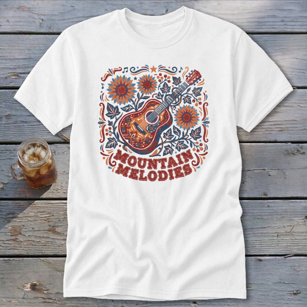 A white t-shirt featuring a folk-art graphic of a guitar, sunflowers, and the text MOUNTAIN MELODIES.