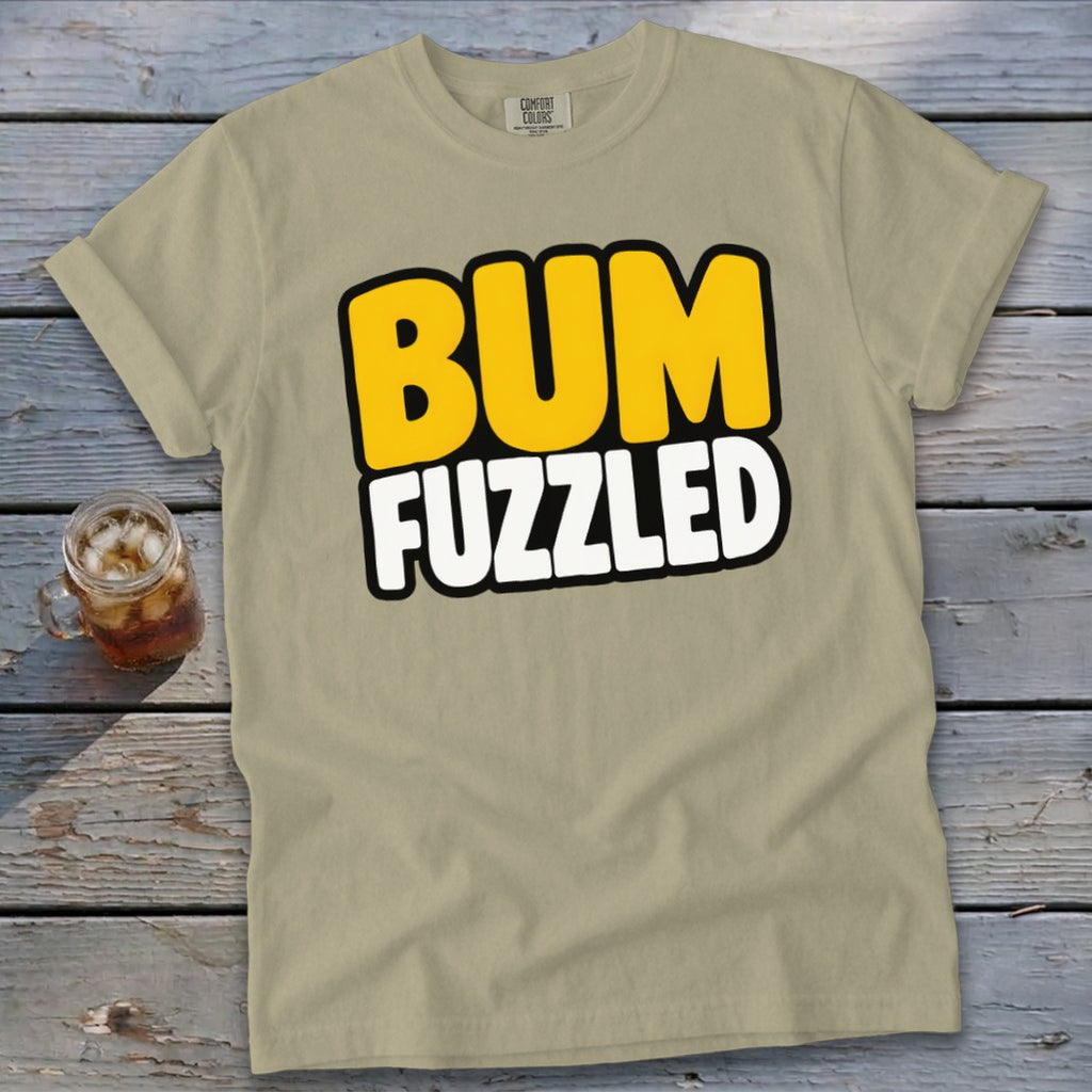 Beige t-shirt featuring the text BUM FUZZLED in yellow and white, laid on a wooden surface.