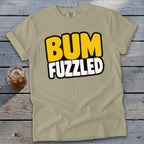 Beige t-shirt featuring the text BUM FUZZLED in yellow and white, laid on a wooden surface.