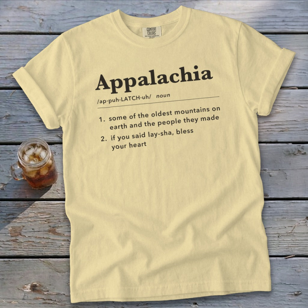 A pale yellow t-shirt with black text defining Appalachia displayed on a wooden surface.