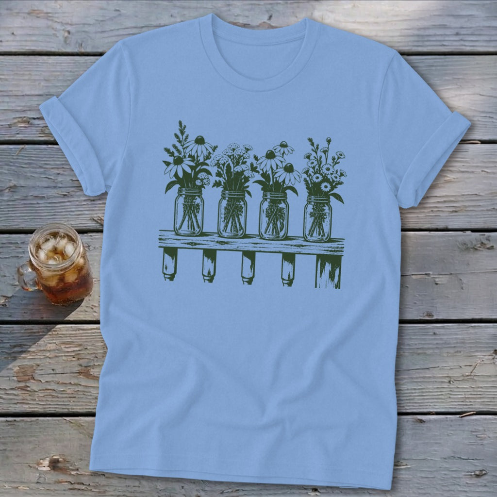 Light blue t-shirt featuring a green graphic of four mason jars filled with wildflowers on a shelf.