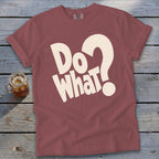 Dusty red t-shirt with cream text reading "Do What?" laid flat on a rustic wooden surface.