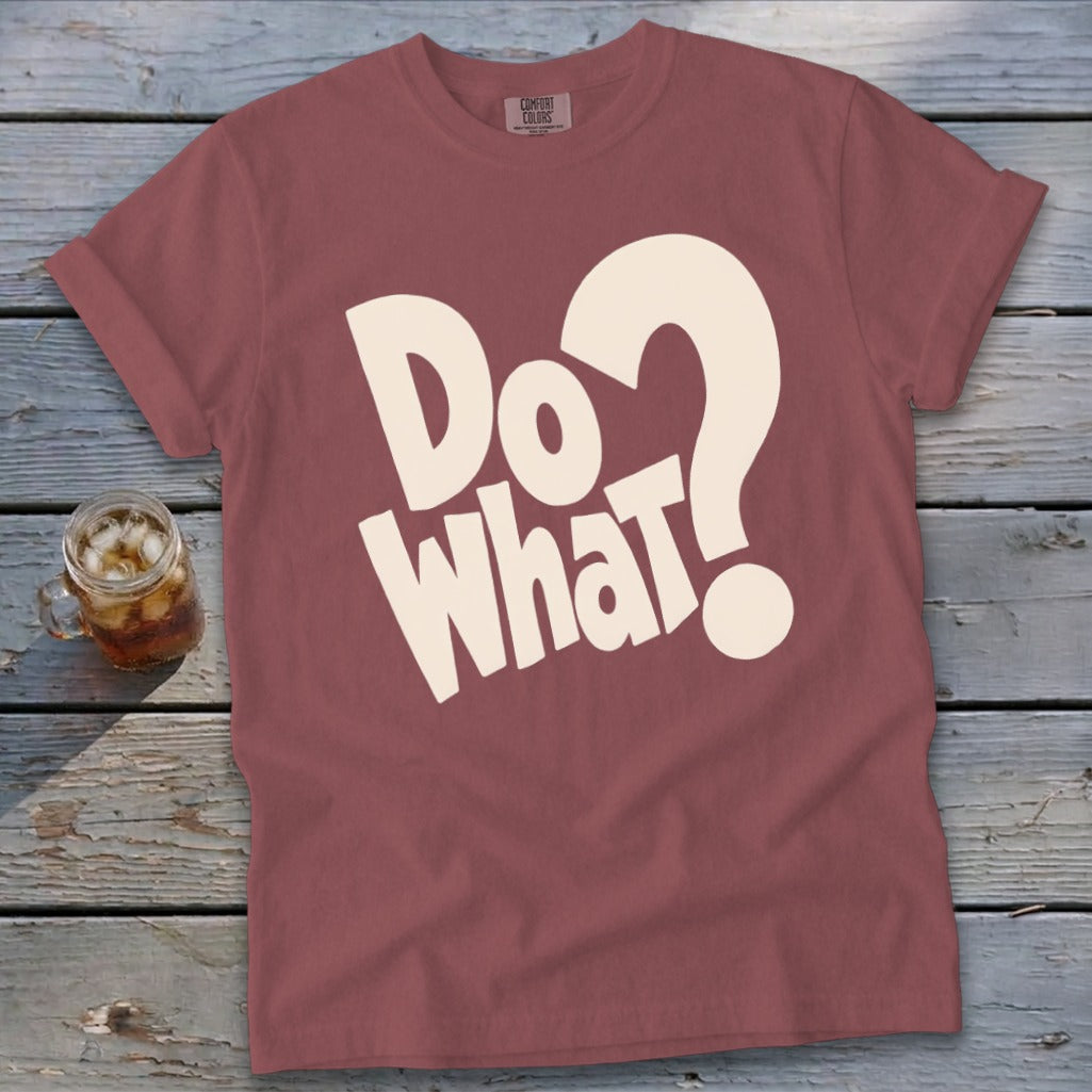 Dusty red t-shirt with cream text reading "Do What?" laid flat on a rustic wooden surface.