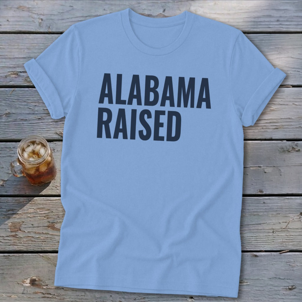 Light blue t-shirt with "ALABAMA RAISED" in dark blue text.