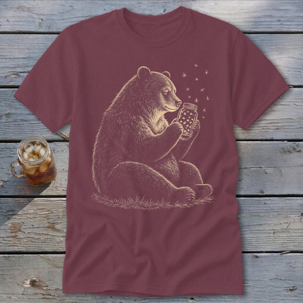 Bear holding a jar of fireflies on a maroon t-shirt.