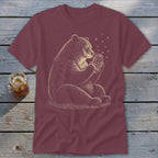 Bear holding a jar of fireflies on a maroon t-shirt.
