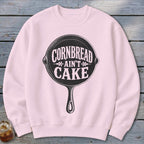 Pink sweatshirt with black graphic of cast iron pan and text "Cornbread Ain't Cake."