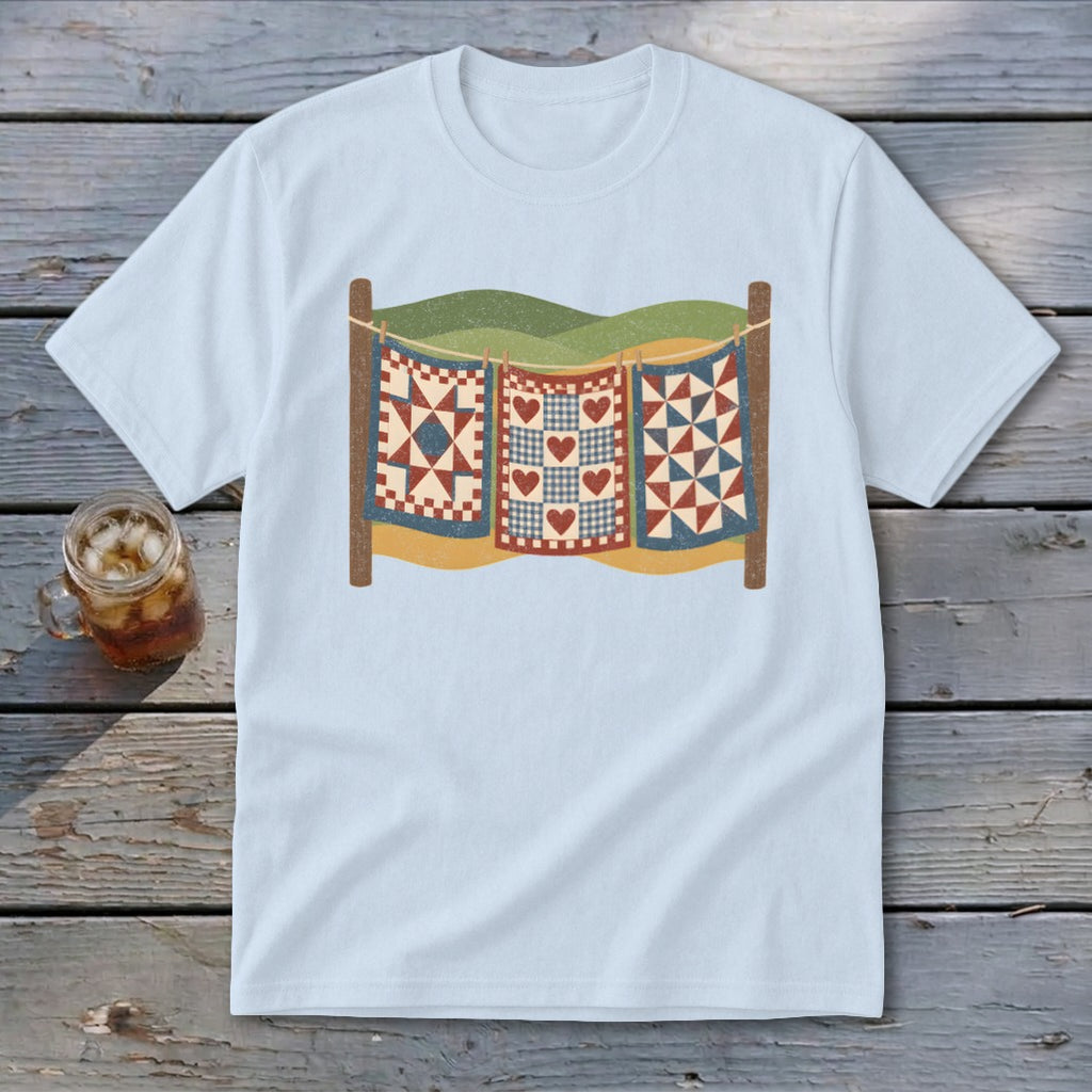 A light blue t-shirt with a graphic of three patchwork quilts hanging on a clothesline.