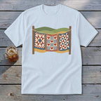A light blue t-shirt with a graphic of three patchwork quilts hanging on a clothesline.