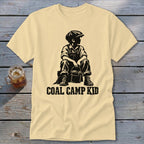 Pale yellow t-shirt with black graphic of a boy in overalls holding a bucket, text "COAL CAMP KID".