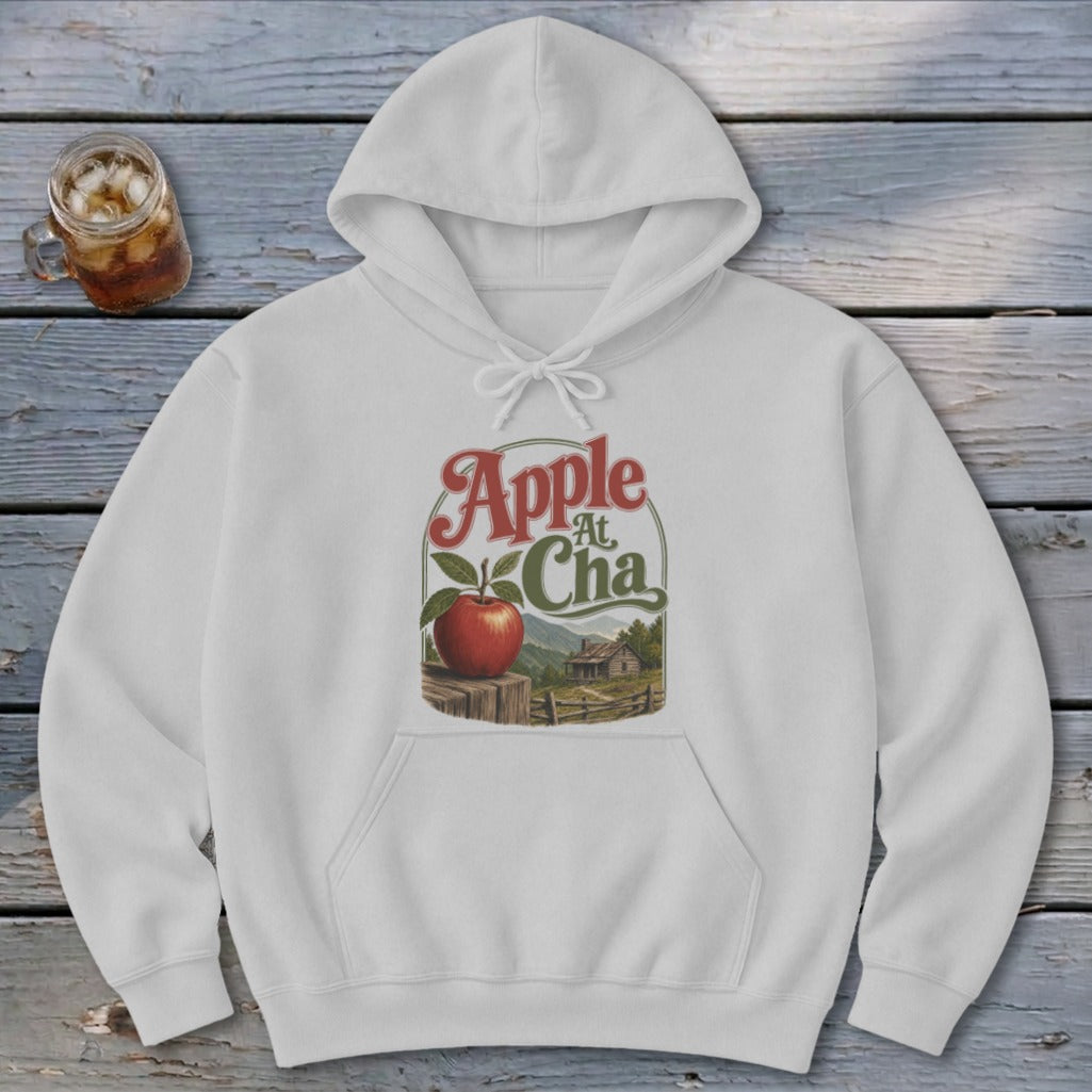 A white pullover hoodie with a graphic of a red apple and a rural landscape scene.