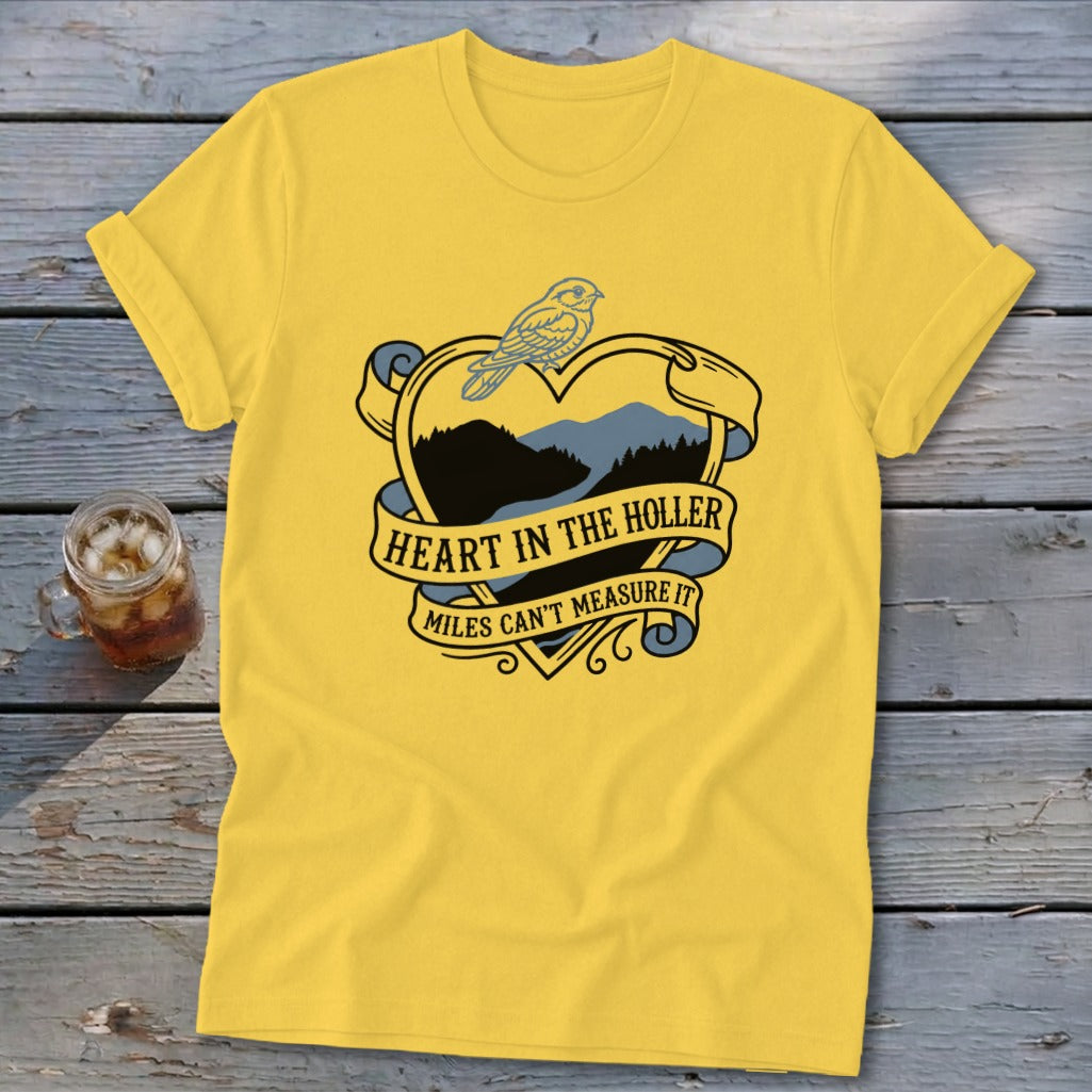 Yellow t-shirt with heart graphic featuring mountains, bird, and text "Heart in the Holler Miles Can't Measure It".