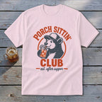 White t-shirt with a distressed graphic of a bear wearing a cap, drinking from a jar. Text reads "Porch Sittin' Club - est. after supper".