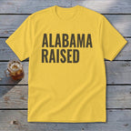 Yellow t-shirt with "ALABAMA RAISED" in dark text.