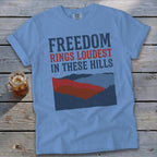 Light blue t-shirt with "FREEDOM RINGS LOUDEST IN THESE HILLS" text and mountain graphic.